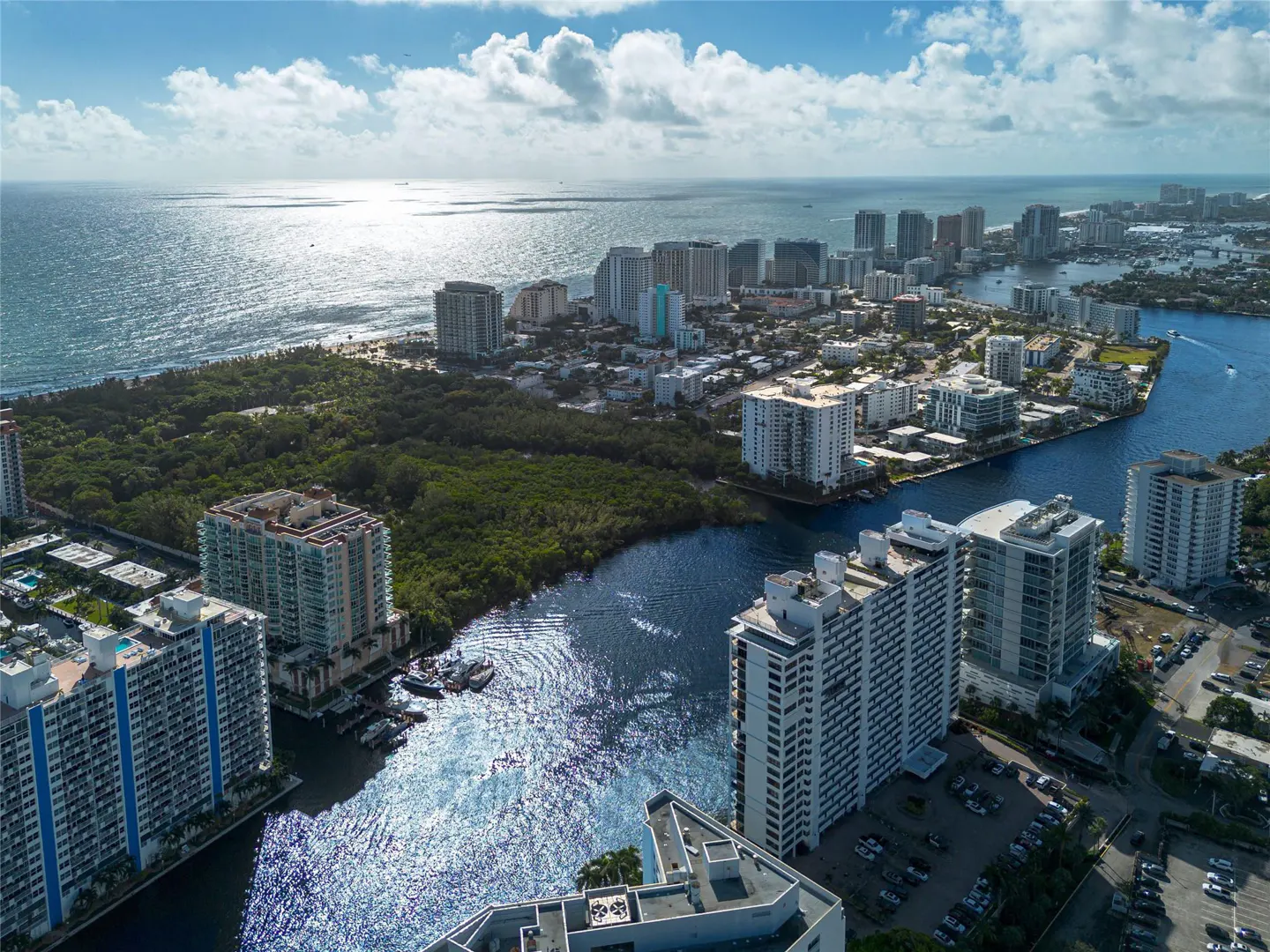 Aerial view of a coastal city with high-rise buildings, a blue waterway, and the ocean under a partly cloudy sky.