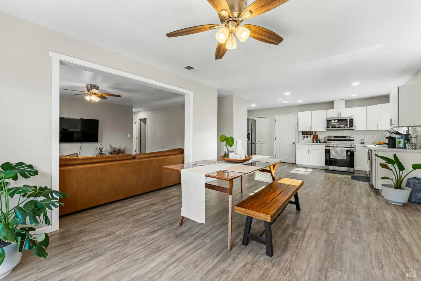 Open-concept home with a dining area, wooden bench, and a view into a living room with a brown leather sofa.