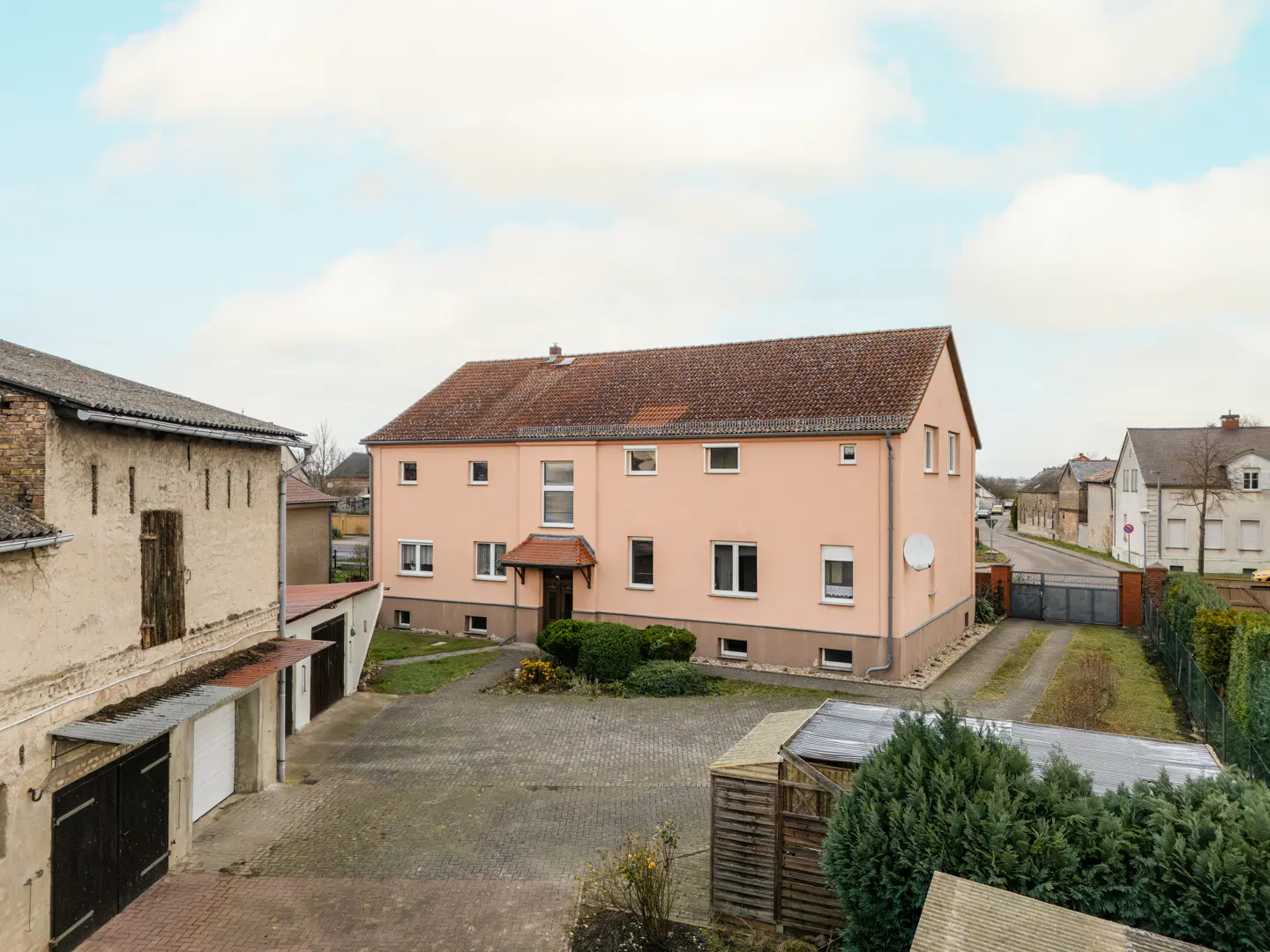 A peach two-story house with a brown roof, a paved driveway, and green bushes.