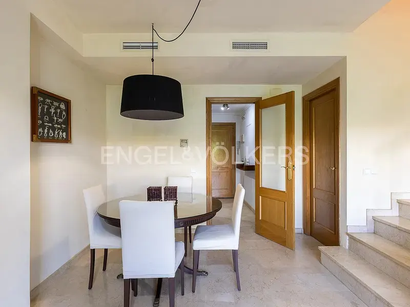 Dining area with a round glass table, four white chairs, a black pendant light, and wooden doors on a marble floor.