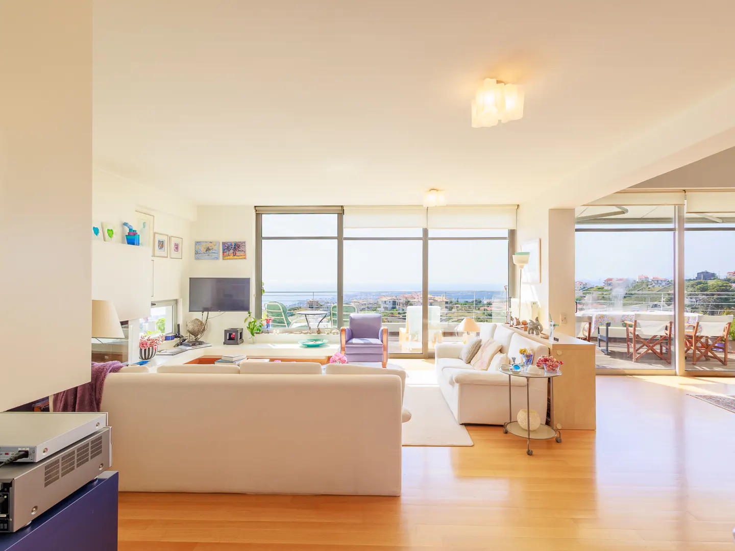 Bright, open living room with hardwood floors, white sofas, and large windows with a scenic view.