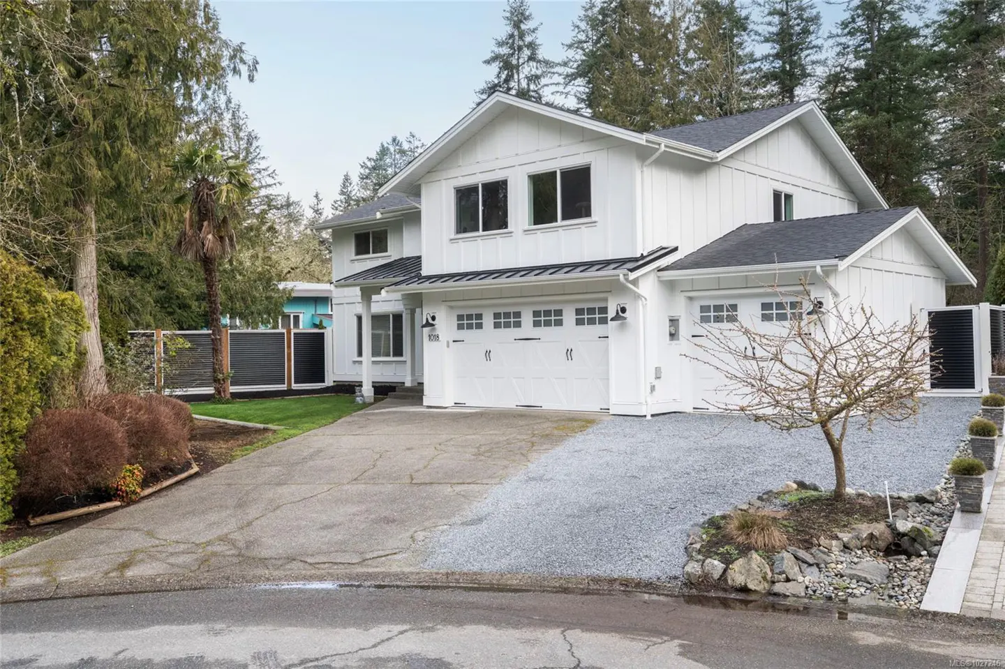 Two-story white house with a black roof, a two-car garage, and a concrete driveway. Trees surround the house.