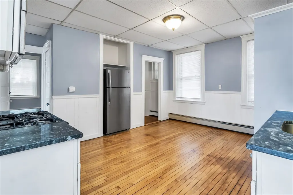 Bright kitchen with hardwood floors, blue walls, and white trim. Stainless steel refrigerator and black gas stove are visible.