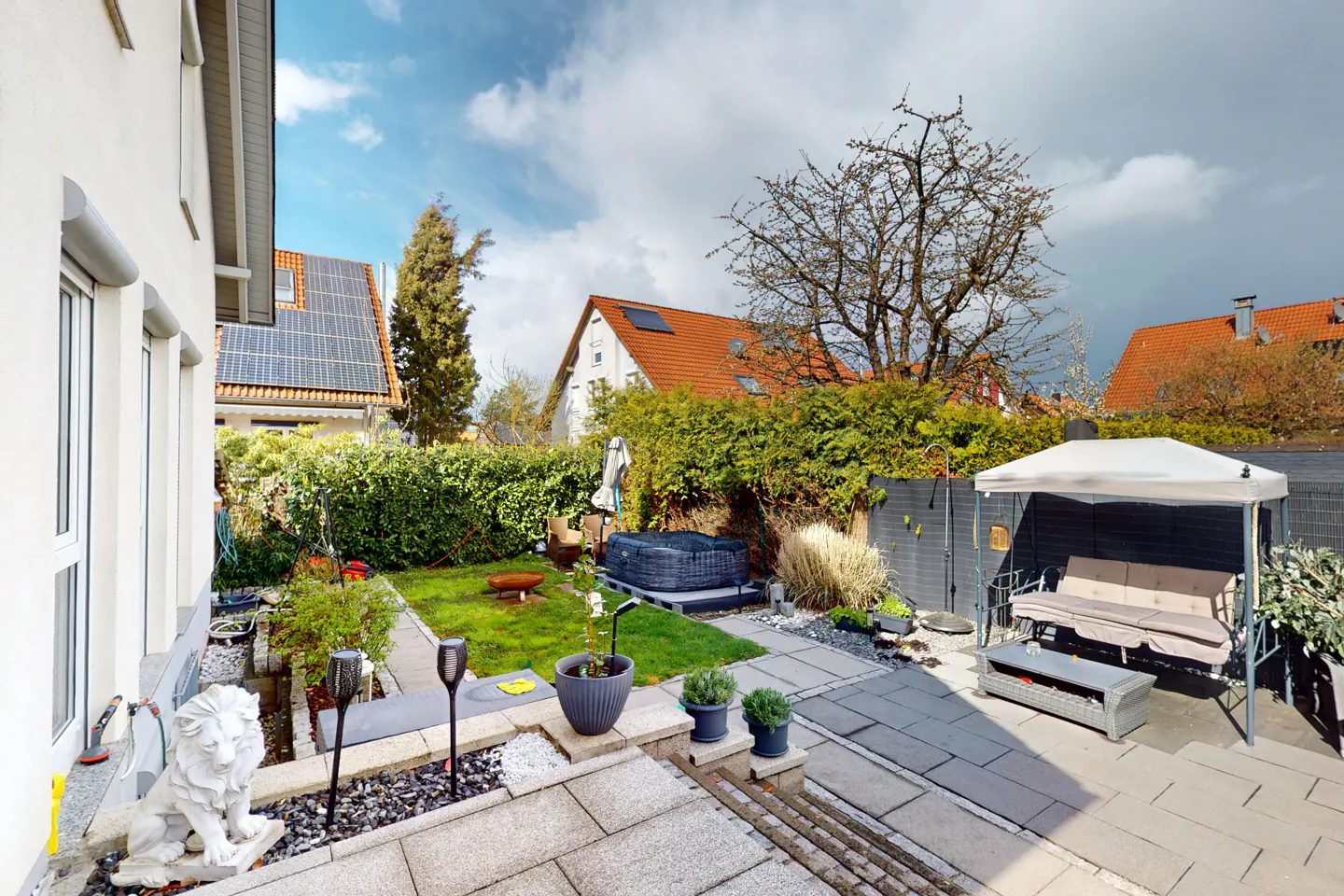 A backyard with a stone patio, green lawn, hot tub, and swing with a canopy.
