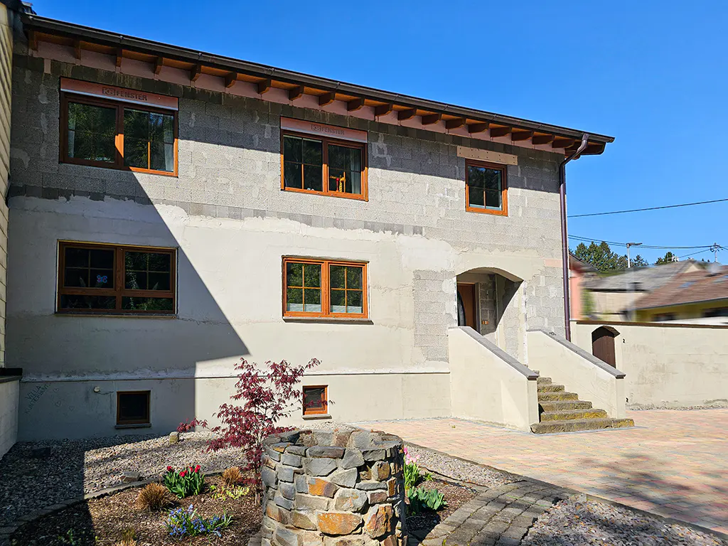 Exterior of a two-story house with gray cinder block and beige stucco, brown-framed windows, and stone well.