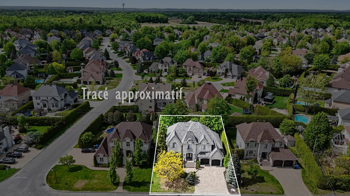 Aerial view of a large, gray stone house with a two-car garage, surrounded by green trees and other houses.