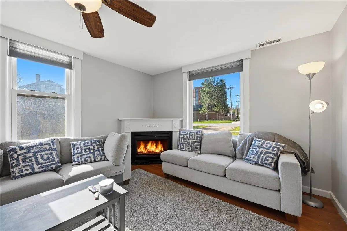 Living room with gray sofas, blue patterned pillows, and a fireplace. A ceiling fan and windows add natural light.