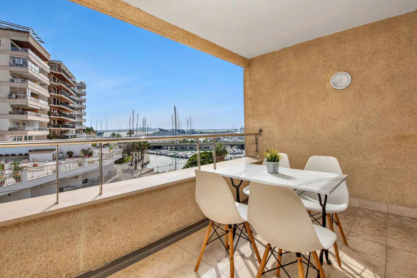 Balcony view with a white table and chairs overlooking a marina with boats and buildings under a blue sky.
