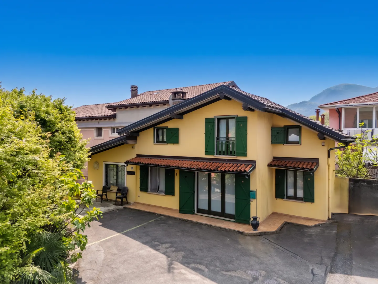Two-story yellow house with green shutters and a brown roof under a clear blue sky.