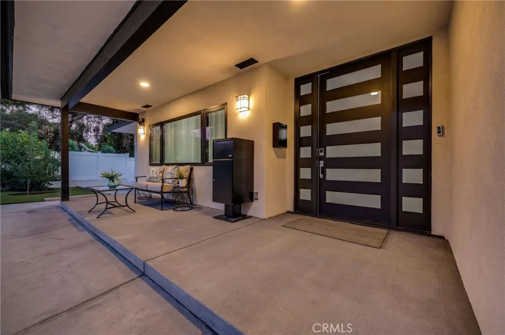Covered porch with a modern black door with glass panels, a black mailbox, and outdoor seating.