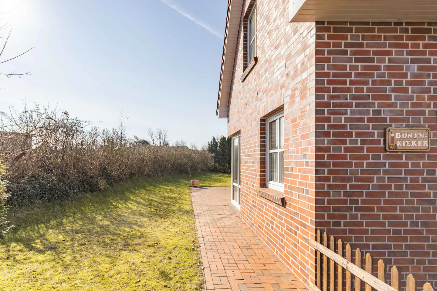 Exterior view of a red brick house with a brick walkway, green lawn, and a sign that reads "Dünen-Kieker".