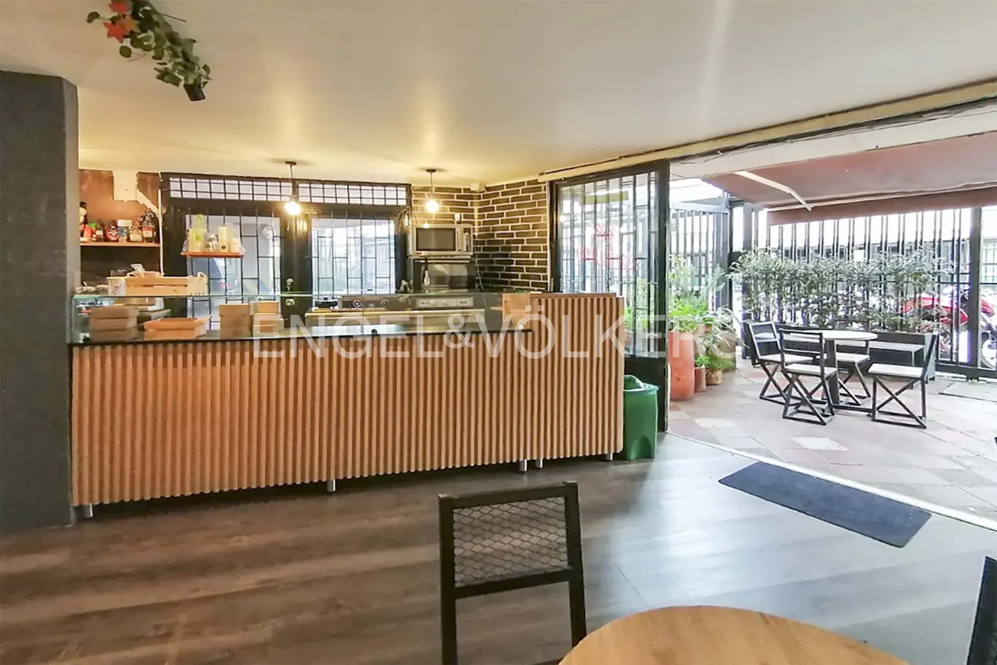 Interior view of a cafe with a wooden counter, tables, and chairs on a patio.