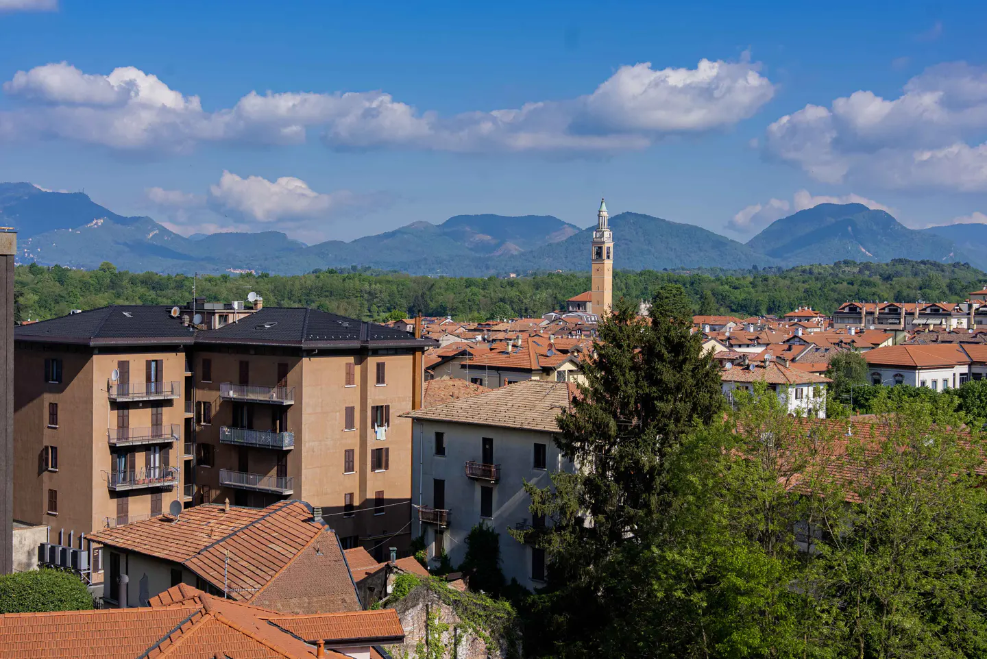 View of a European town with red-tiled roofs, a tall church tower, and mountains in the background.