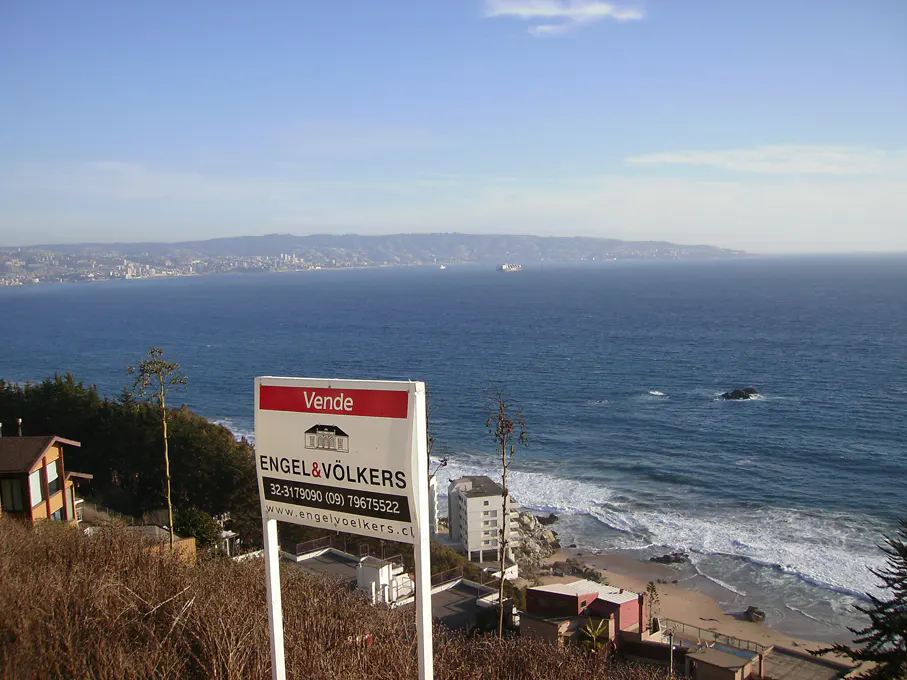 Ocean view property for sale. Engel & Völkers sign in foreground, blue ocean and coastline in background.