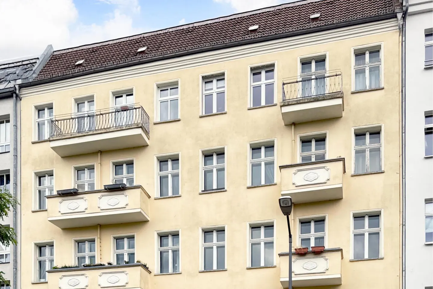 A light yellow apartment building with white framed windows and small balconies. The roof is brown.