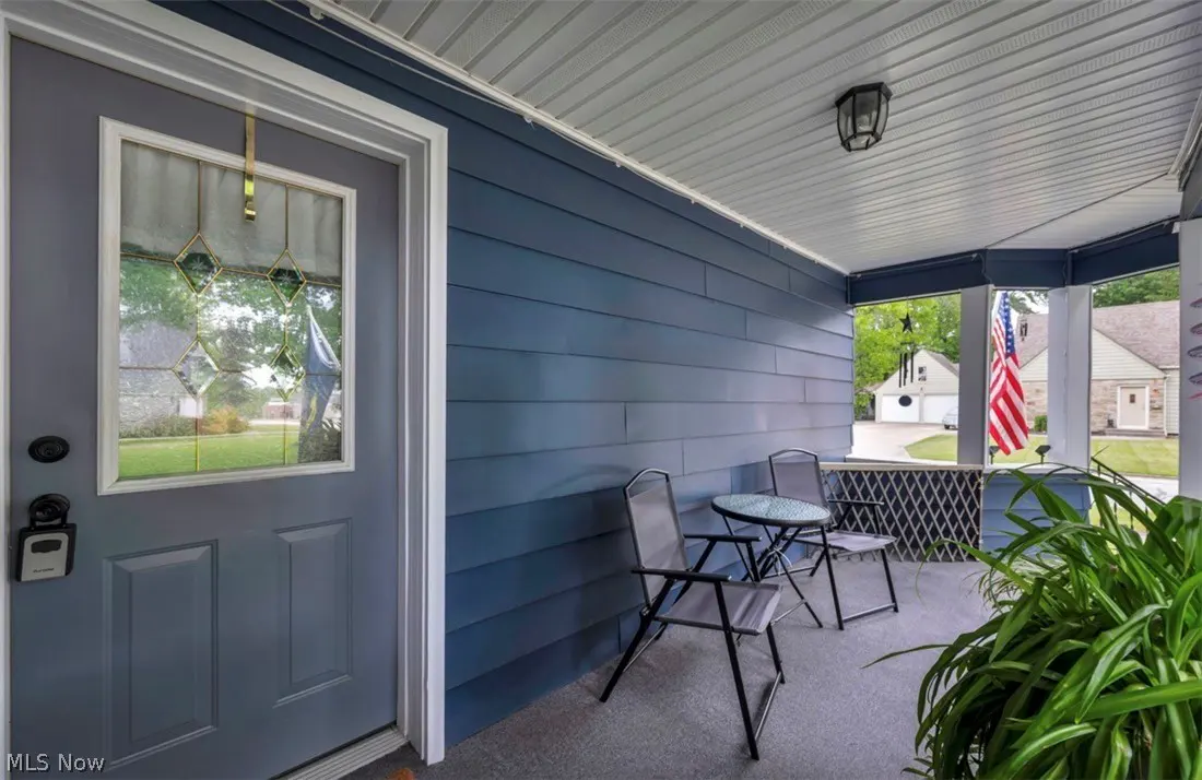 Covered porch with blue siding, a gray front door with diamond-patterned glass, and a small table with two chairs. An American flag is visible.