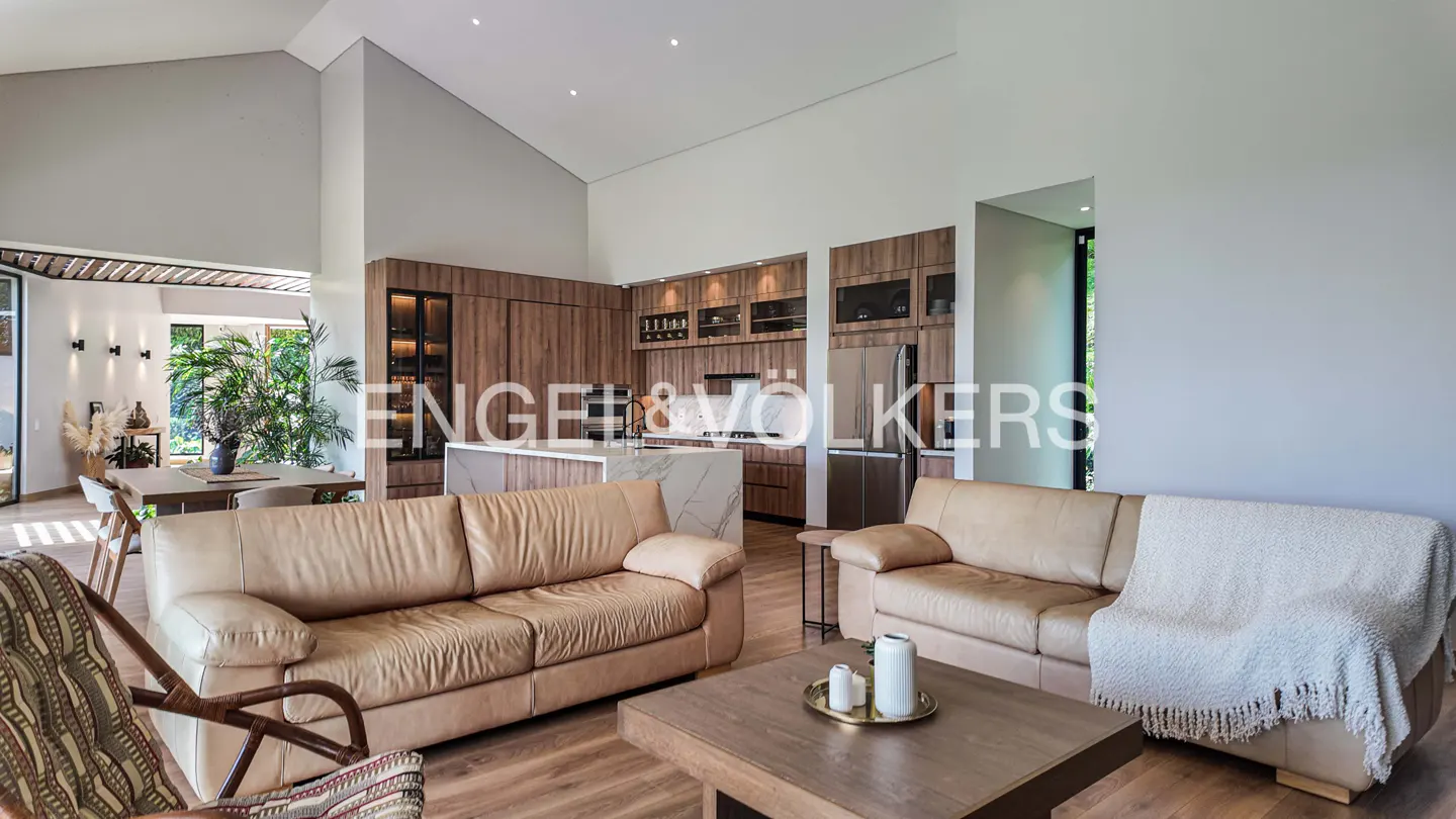 Open-concept living space with tan leather sofas, wood floors, and a kitchen with wood cabinets and a marble island.