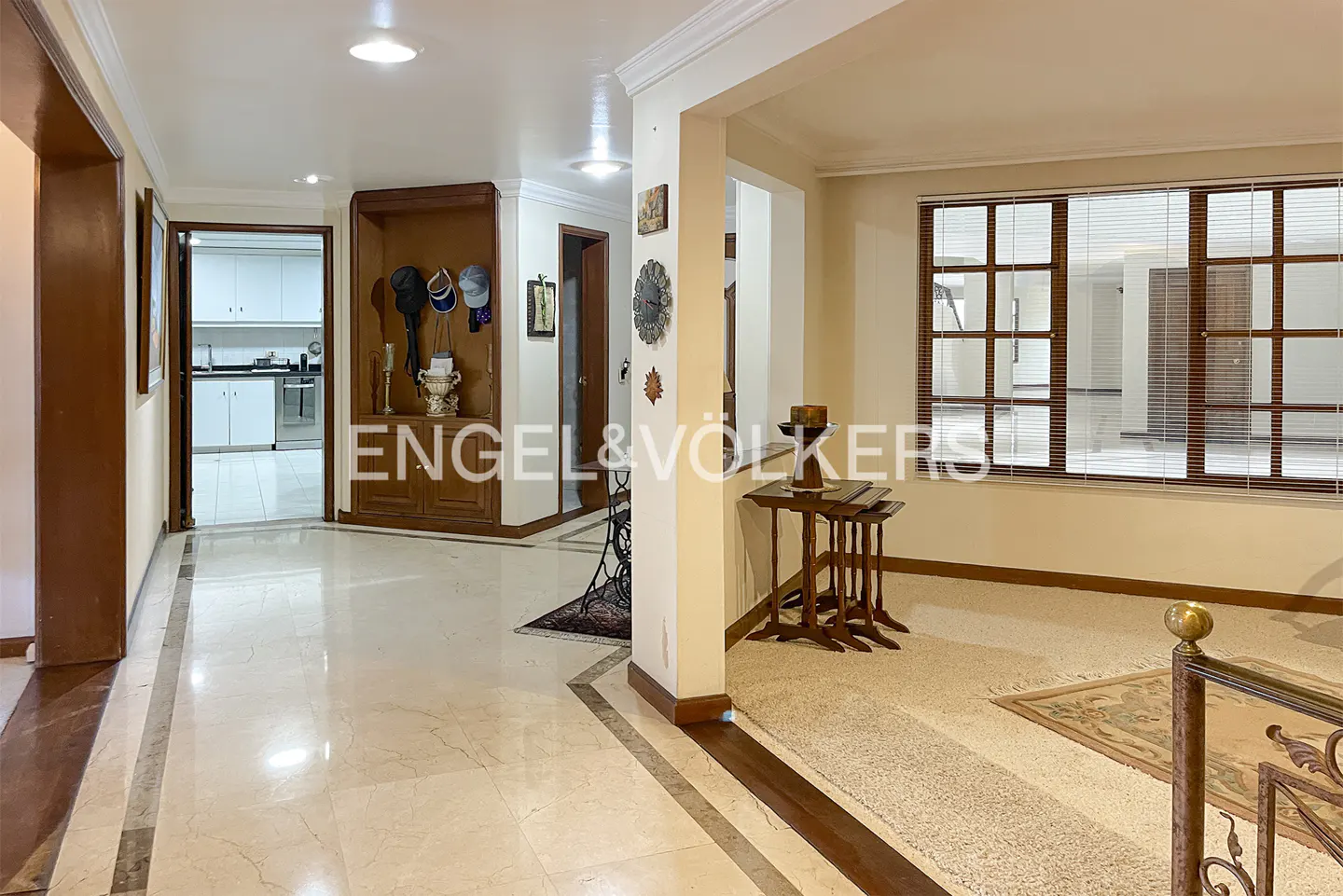 A bright foyer with marble floors leads to a living room with a large window and a view of the Engel & Völkers logo.