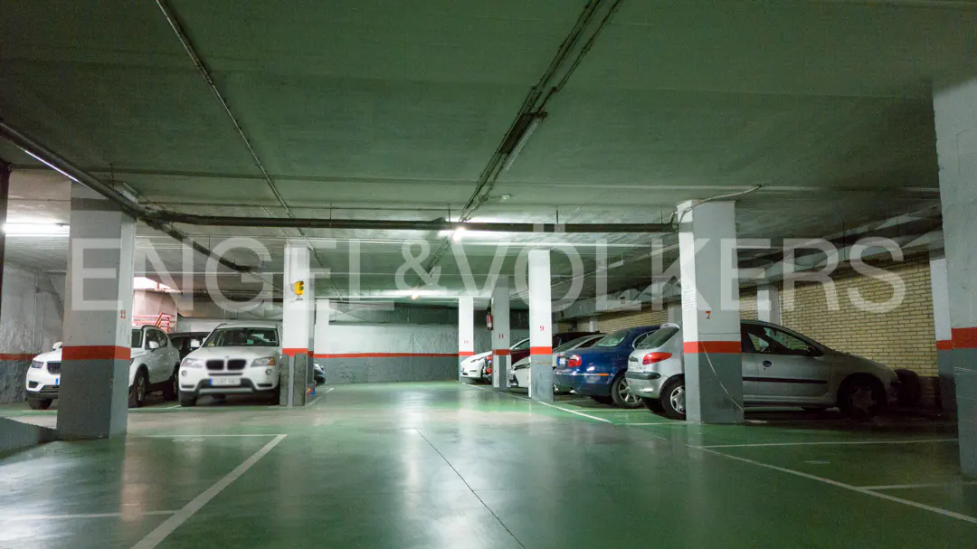 Indoor parking garage with several parked cars, white pillars, and green floor.