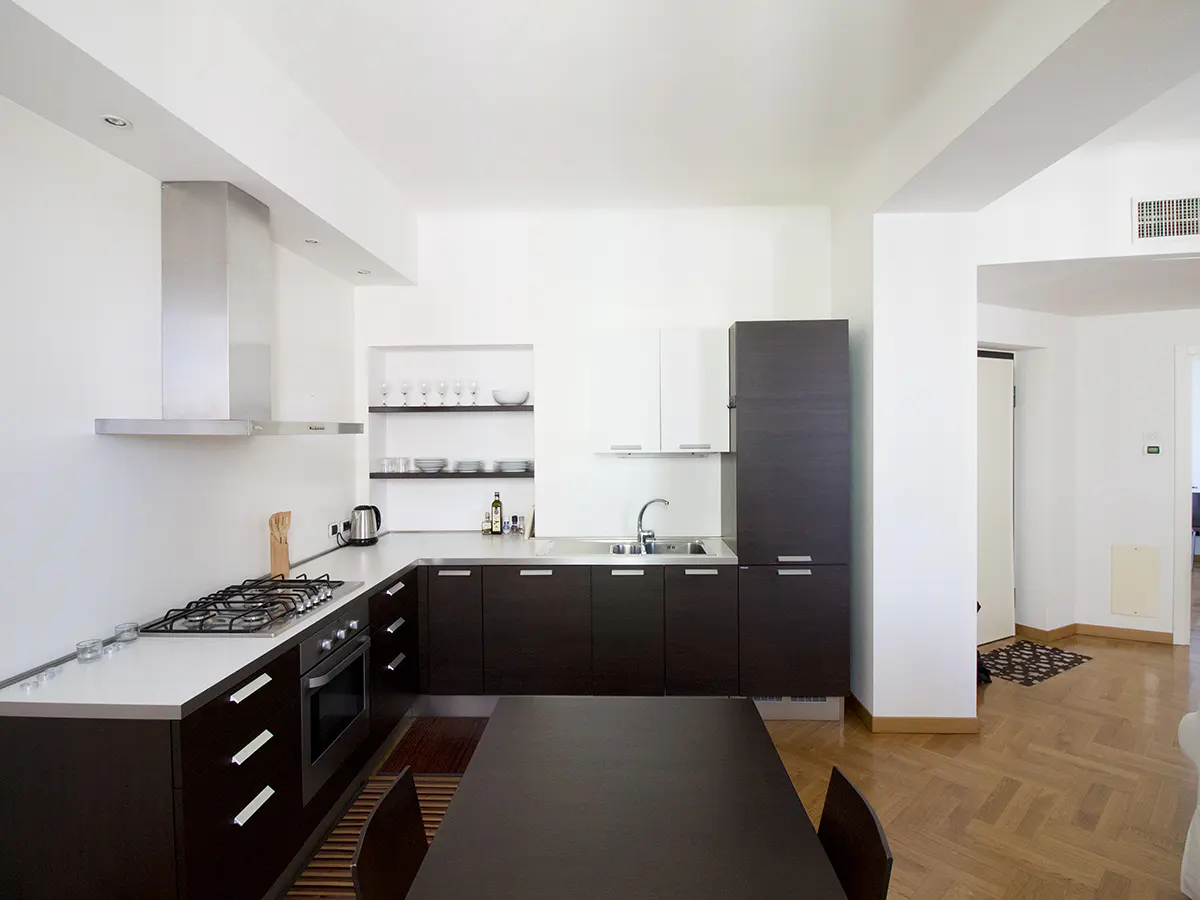 Modern kitchen with dark wood cabinets, white walls, stainless steel appliances, and a dark wood table with chairs.