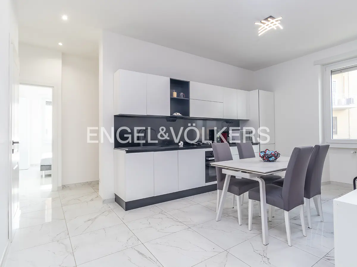 A bright, modern kitchen with white cabinets, black countertops, and a dining table with gray chairs. Marble floors add elegance.