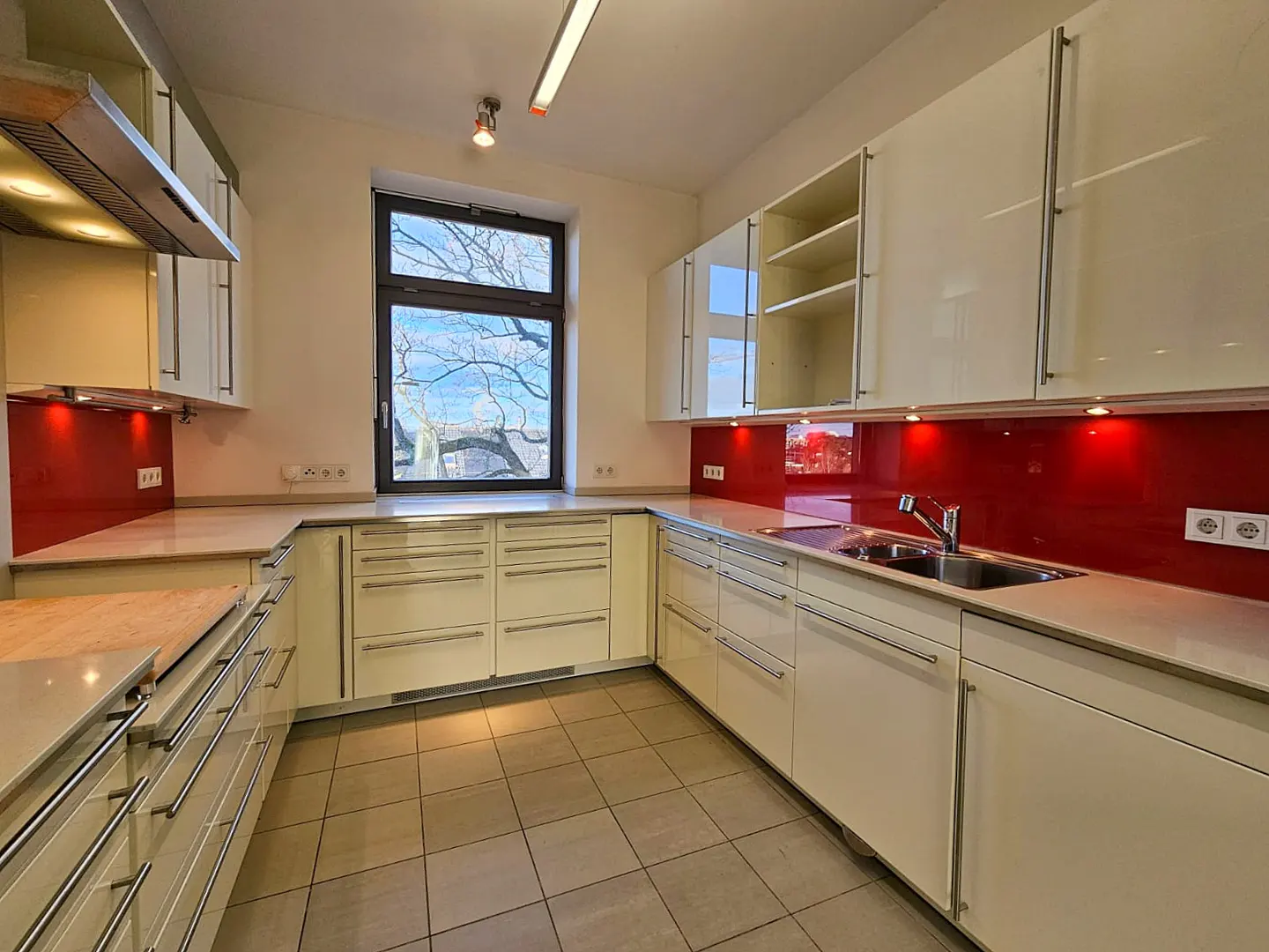 Bright kitchen with cream cabinets, red backsplash, and stainless steel accents. A window overlooks a tree.