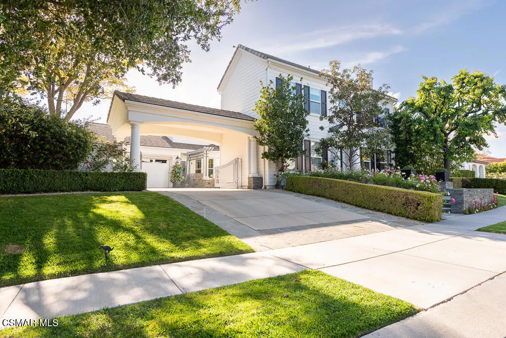 Exterior of a two-story white house with black shutters, a porte-cochère, and manicured landscaping.