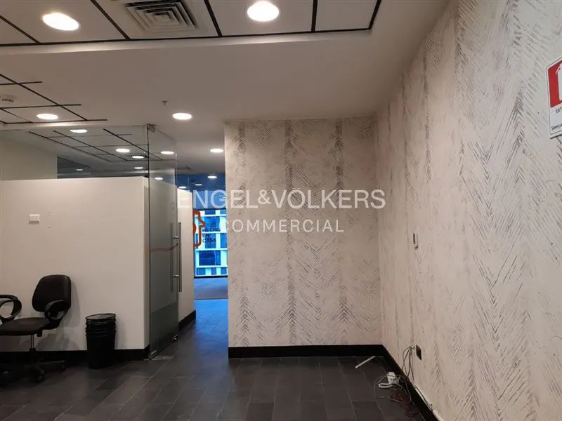 Office space with black tile floor, patterned wallpaper, and glass-walled offices. Engel & Volkers logo on the wall.