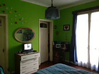 A bedroom with green walls, a blue bedspread, and a white dresser with a small TV on top.