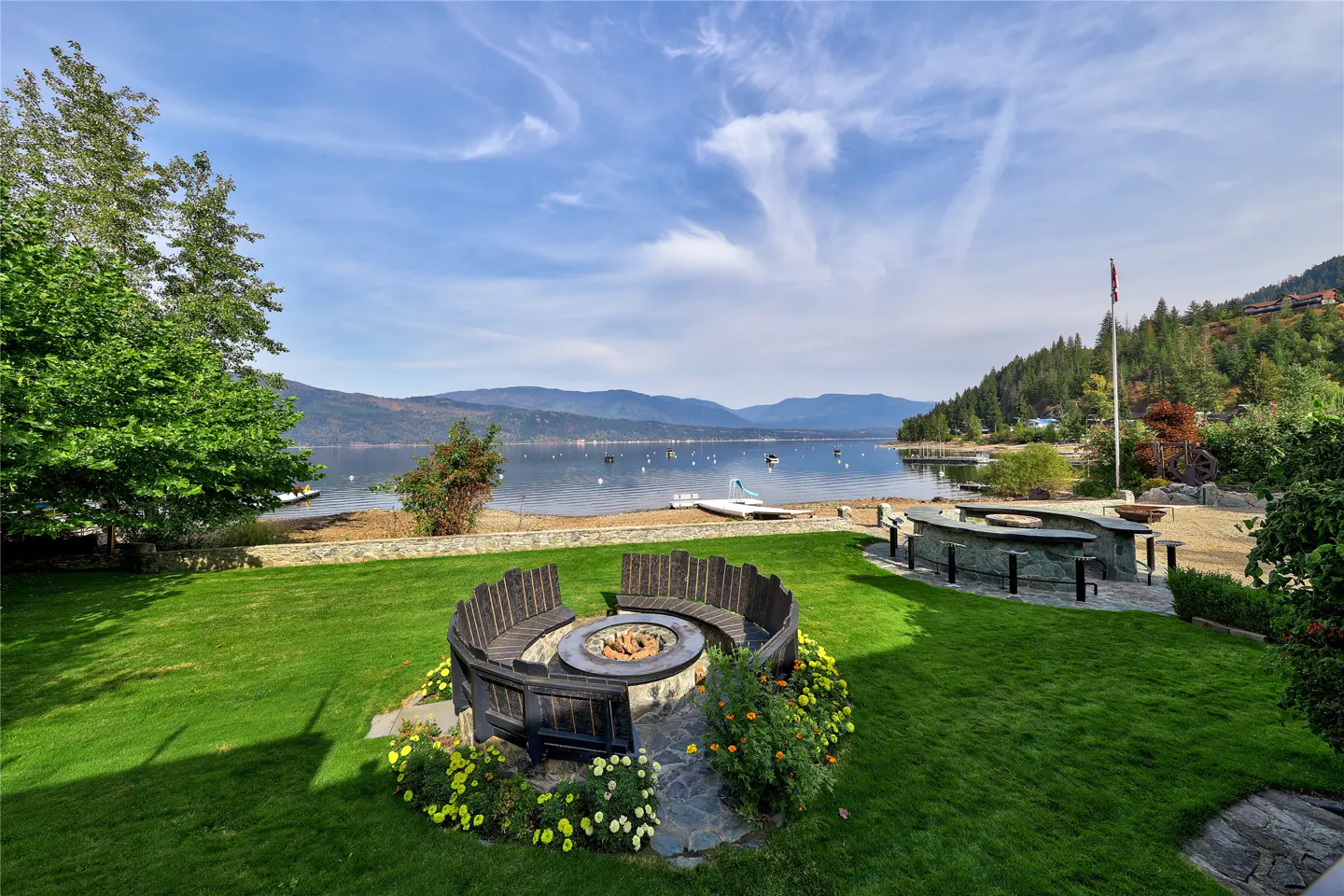 Lawn with a fire pit and seating area overlooking a lake and mountains under a blue sky.