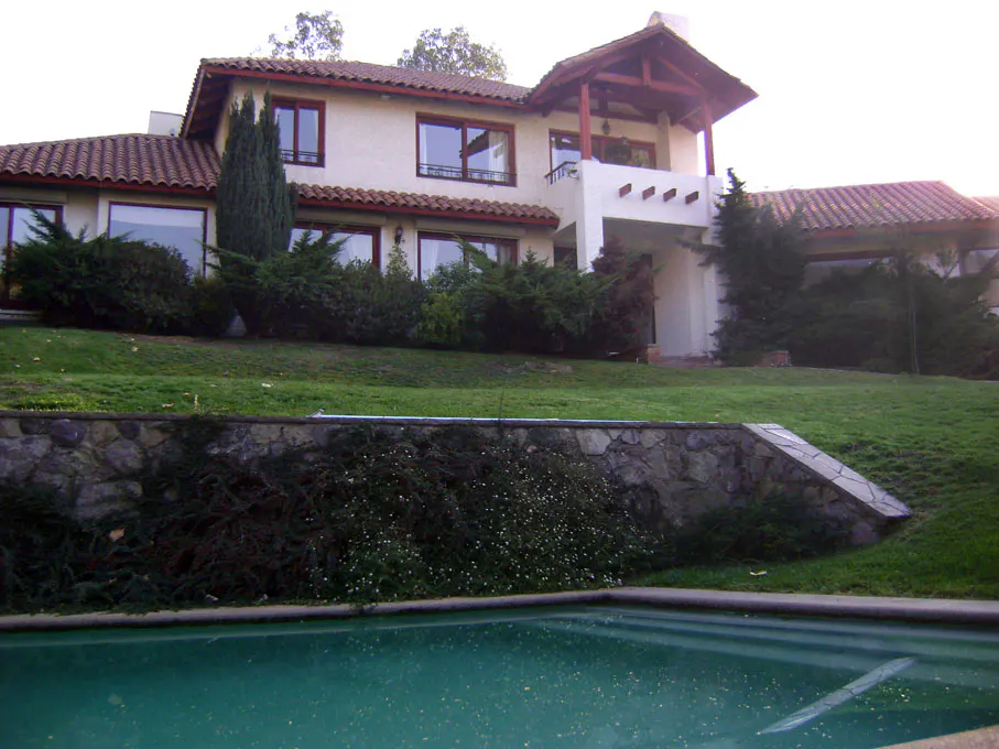 Two-story house with a red tile roof, white walls, and a green lawn, viewed from the pool.