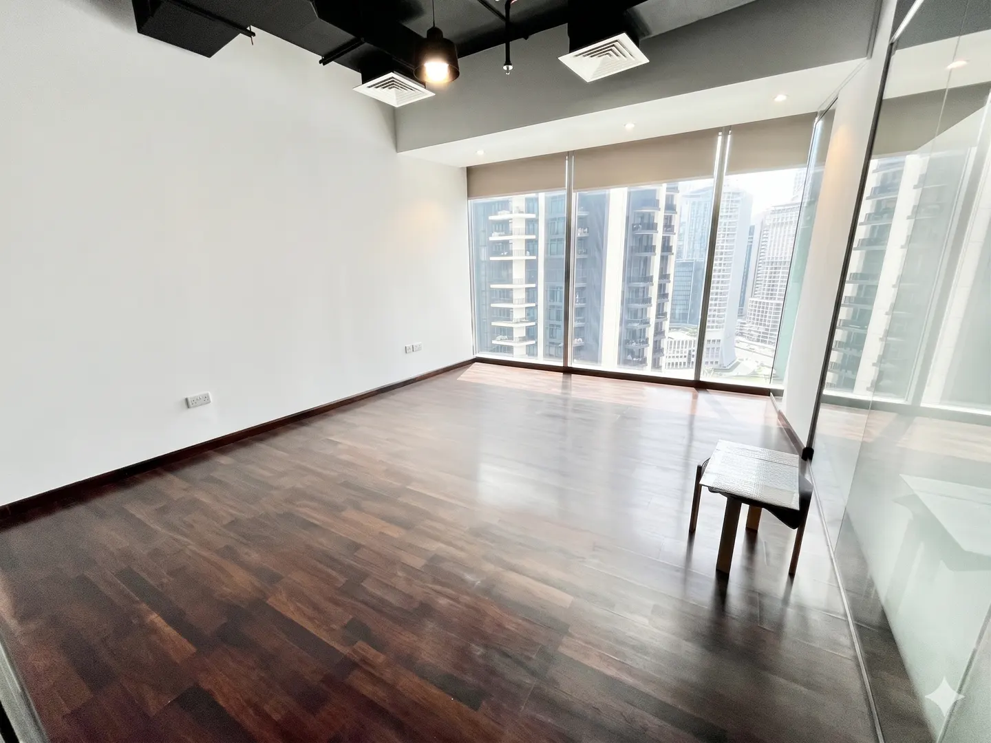 Empty room with dark wood floors, white walls, and a large window with a city view.