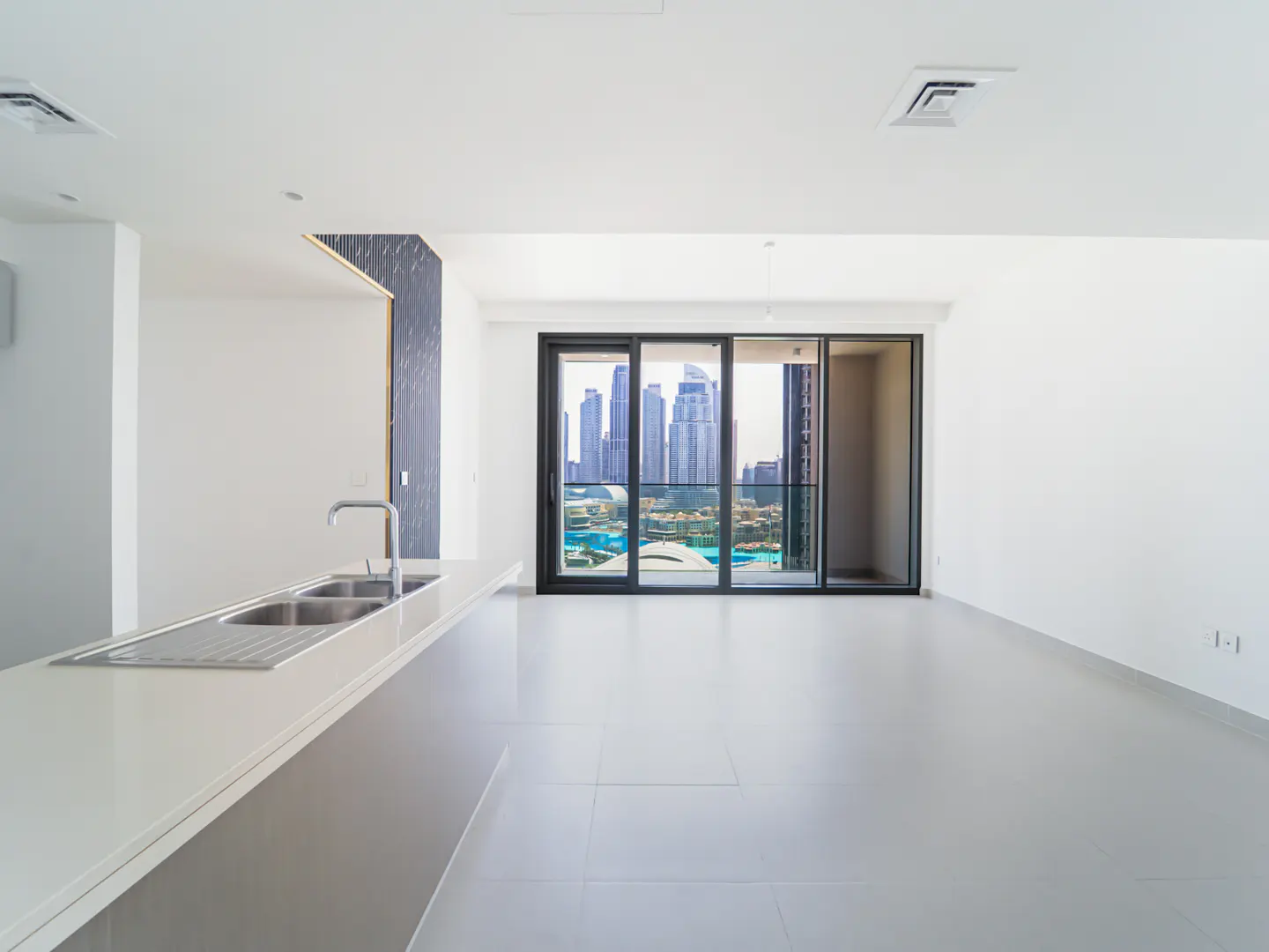 A bright, empty apartment with a kitchen island and a view of a city skyline through sliding glass doors.