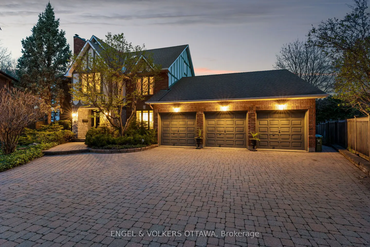Exterior view of a two-story brick house with a three-car garage and a brick driveway at dusk.