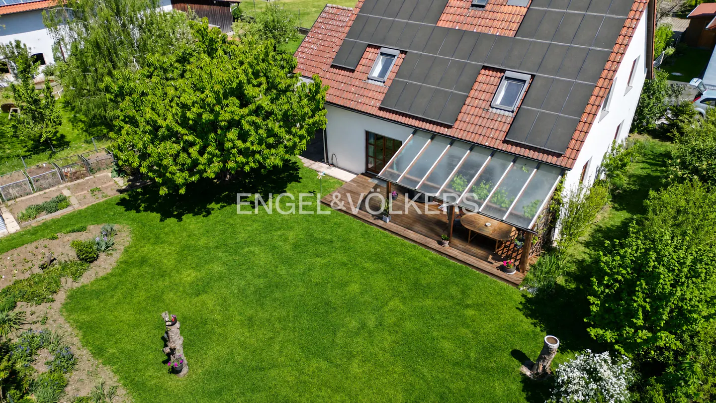 Aerial view of a white house with solar panels, a glass-roofed patio, and a large green lawn.