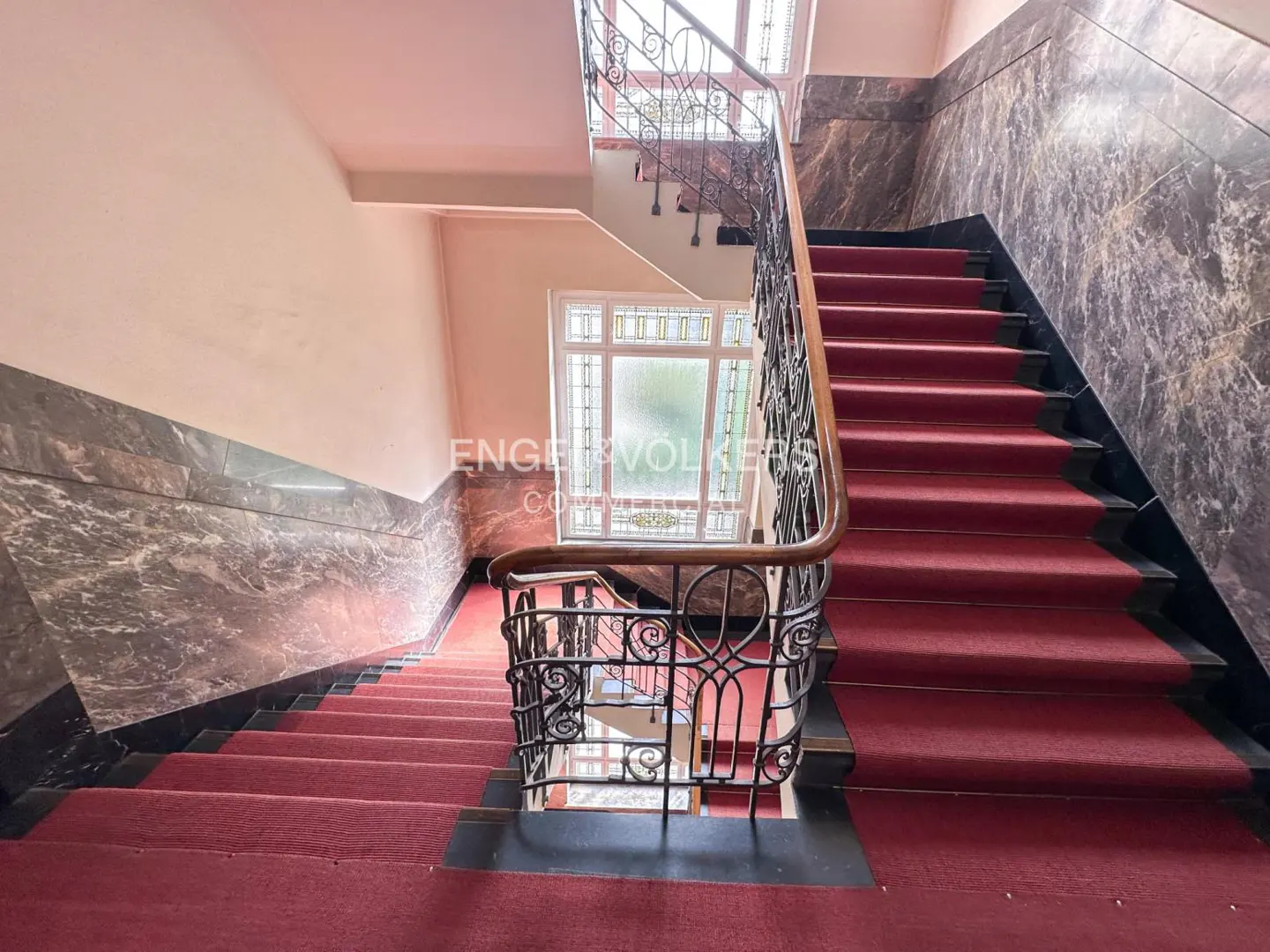 A staircase with a red carpet and black marble walls. A window is visible on the landing.