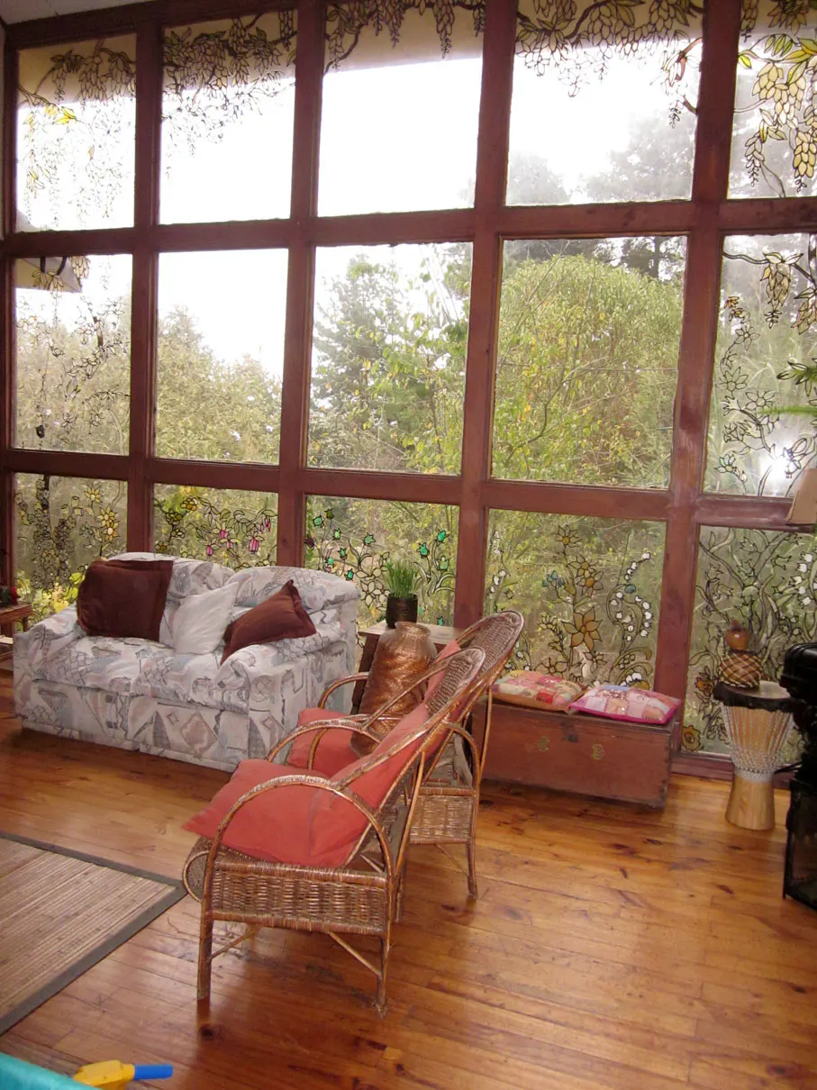 Living room with a large window view of trees. A couch, chairs, and wooden floors are visible.