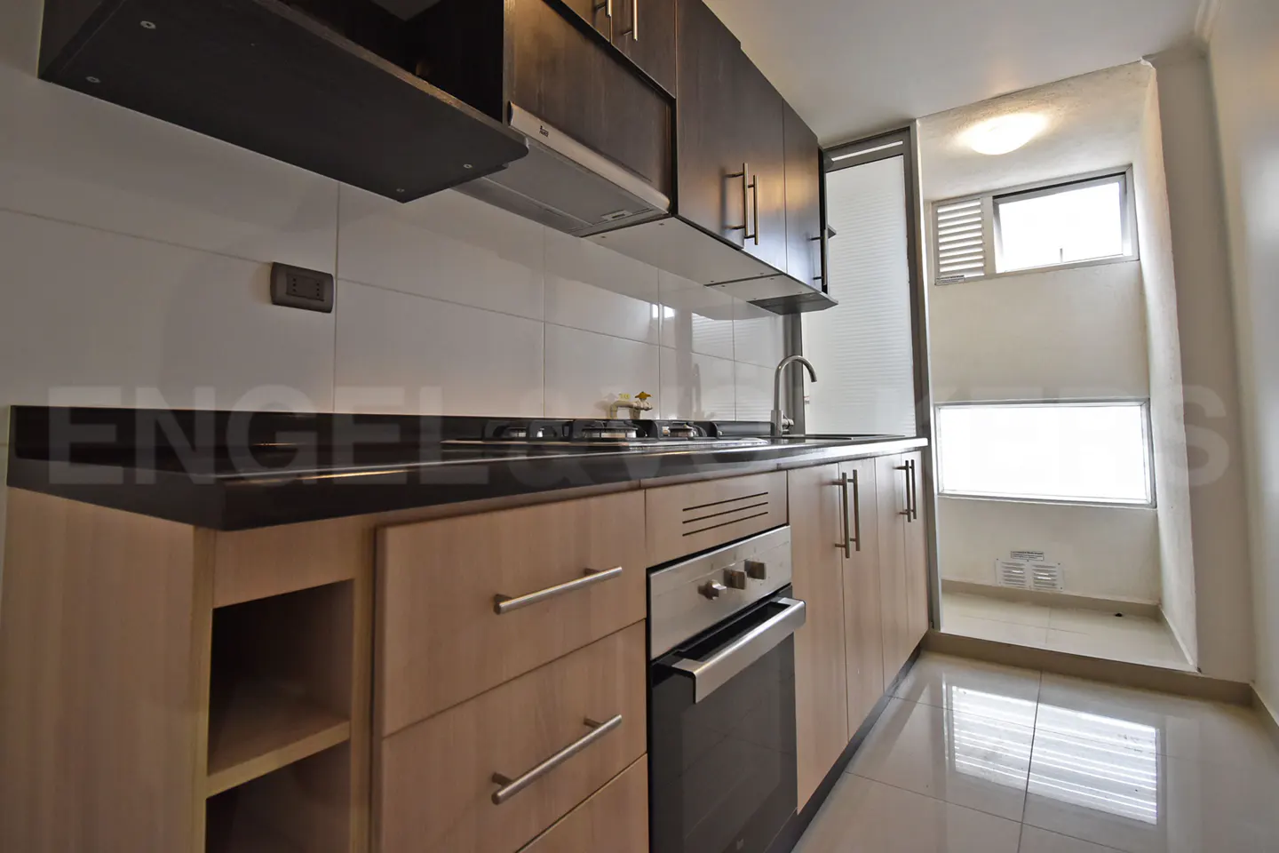 A modern kitchen with light wood cabinets, black countertops, and stainless steel appliances. A bright window is visible in the background.