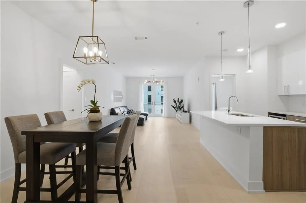 Bright, open-concept living space with a dining table, kitchen island, and living room. White walls and light wood floors create a modern feel.