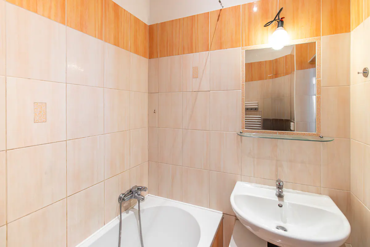 Bathroom with white tub, sink, and orange-and-beige tiled walls. A mirror hangs above the sink with a light fixture above it.