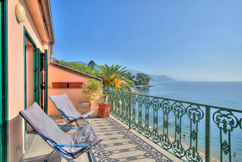 Balcony view with two chairs overlooking the ocean. Green ornate railing, peach building, and blue sky.