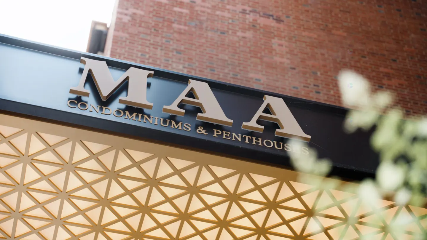 Exterior shot of MAA Condominiums & Penthouses sign in gold lettering on a black background, with a geometric patterned facade below.