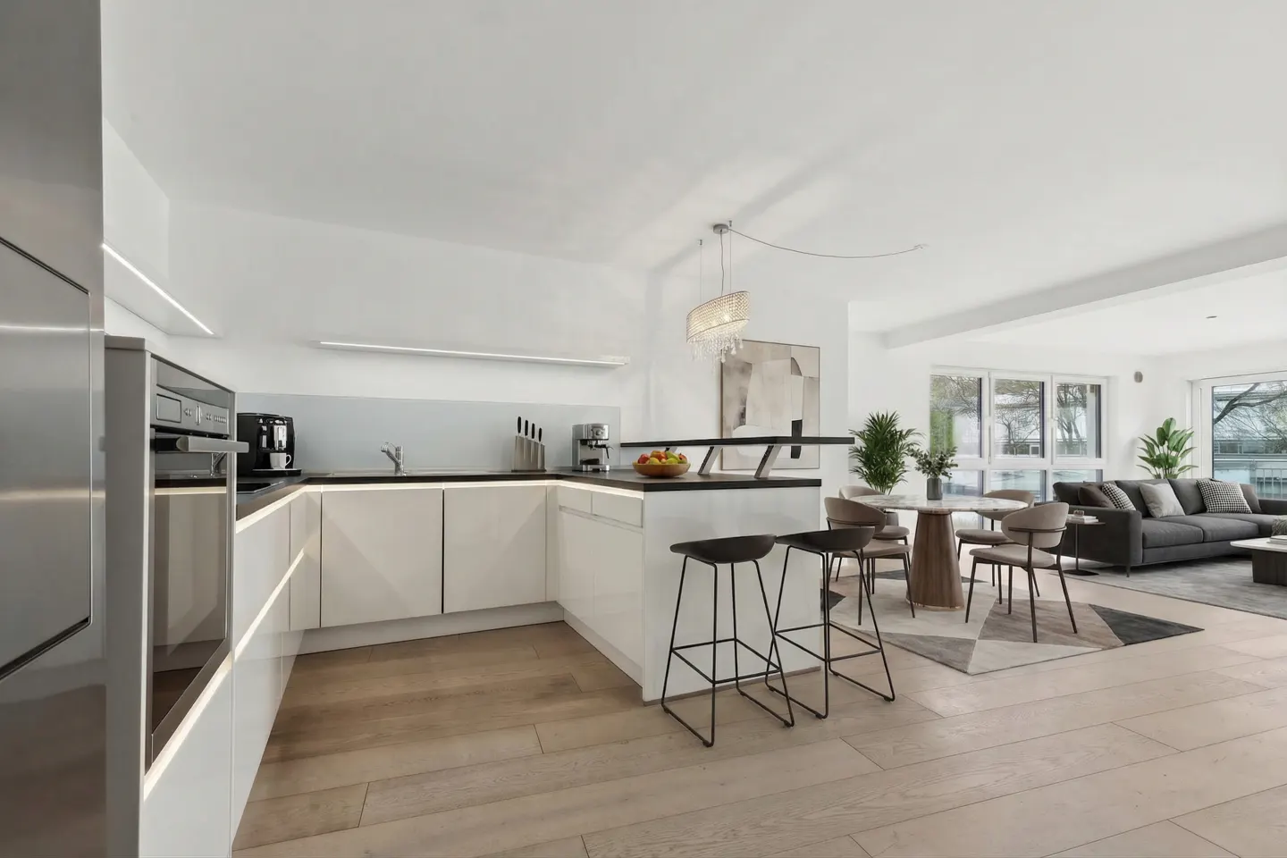 Open-concept kitchen and living room with white cabinets, black countertops, and wood floors. Three black stools at the kitchen island.