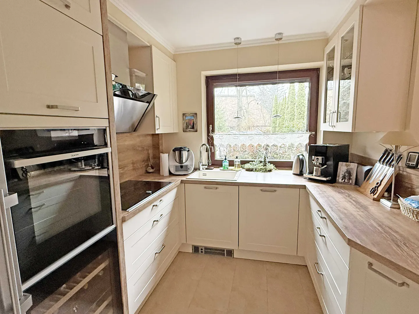 A bright kitchen with cream cabinets, wood countertops, and stainless steel appliances. A window overlooks a garden.
