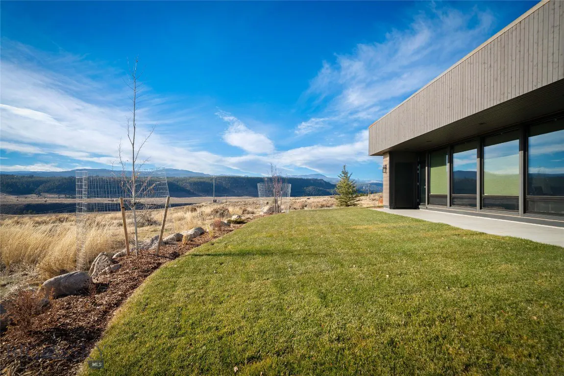 Exterior view of a modern home with a green lawn, mountains, and a blue sky with clouds.