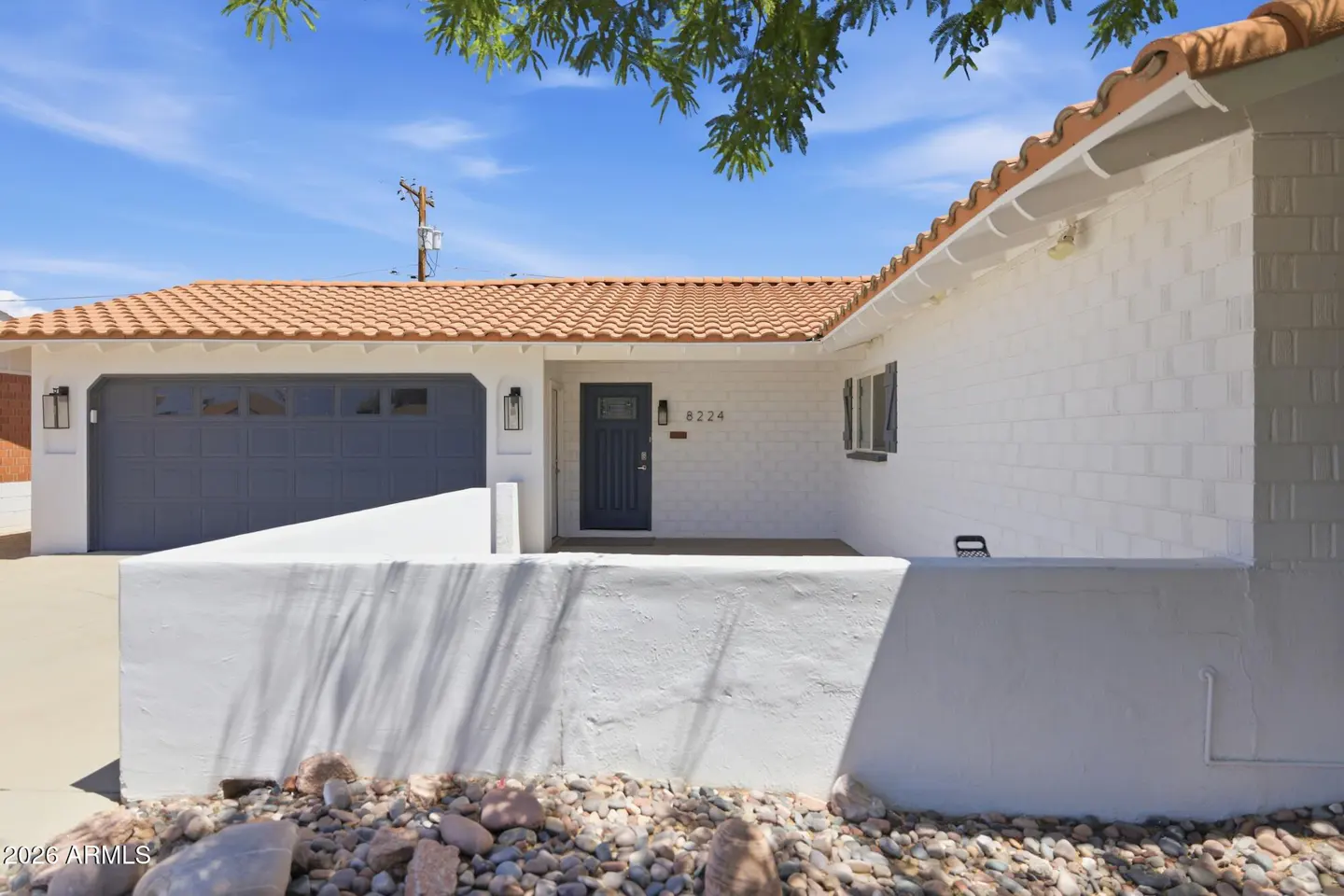 White single-story home with a terracotta tile roof, dark blue garage door, and matching front door under a blue sky.