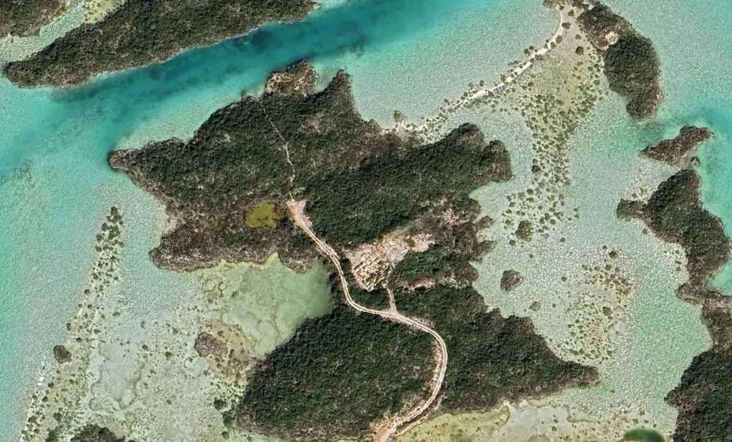 Aerial view of a lush green island surrounded by turquoise water, with a winding dirt road cutting through the trees.