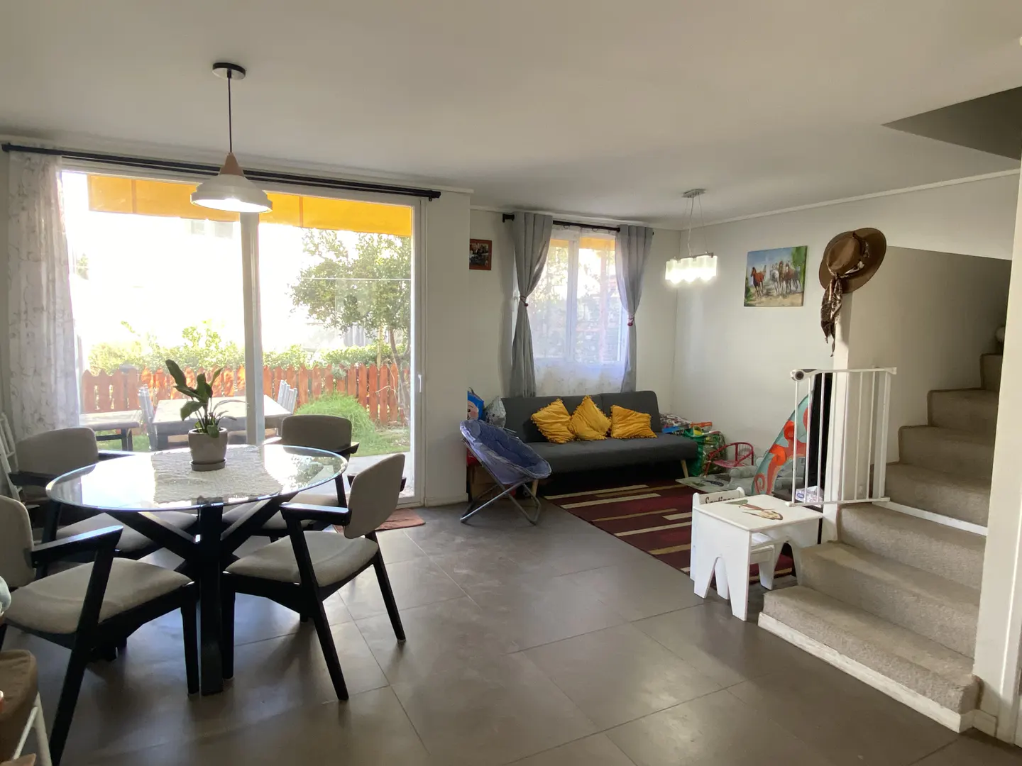 Open-concept living space with a glass dining table, gray sofa with yellow pillows, and stairs with a child safety gate.