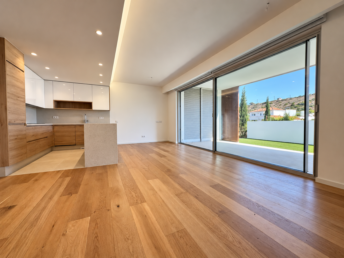 Modern open-plan kitchen with wood cabinets and white counters, featuring large sliding glass doors opening to a patio. [AI-generated text] [AI-modified]