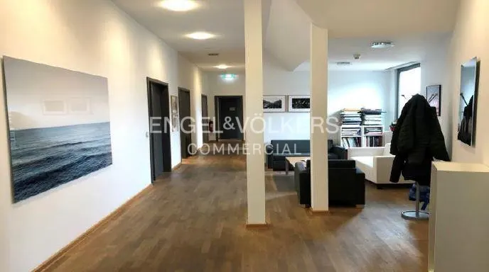 Modern office hallway with wood floors, a large ocean art piece, dark seating area, and a coat rack near the entrance.